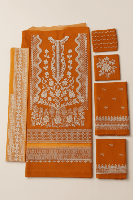 An orange unstitched fabric dress material with intricate white embroidery, including a heavily embroidered neckline and floral patterns, accompanied by matching embroidered panels for sleeves and borders