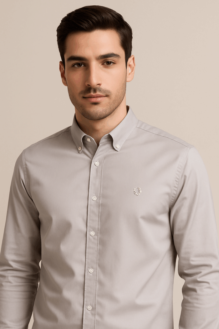 A  light-colored, possibly beige or light grey, long-sleeved cotton shirt with a button-down collar and buttoned cuffs.