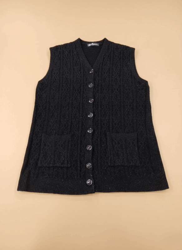 Women's black cable knit sweater vest with buttons and pockets on a beige background