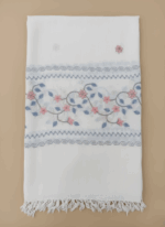 White embroidered floral shawl with pink and blue flower and leaf patterns and fringed edges.