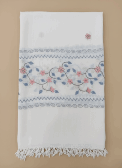 White embroidered floral shawl with pink and blue flower and leaf patterns and fringed edges.