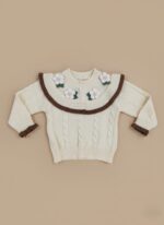 Happy baby in ivory cable knit baby sweater with floral collar and ribbed leggings, brown Mary Jane shoes.