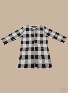 Women's black and white plaid knit sweater with a checkered pattern, long sleeves, toggle closure, and front pockets, displayed against a light brown background.
