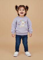 Toddler girl smiling in a purple bunny graphic sweater and blue jeans.