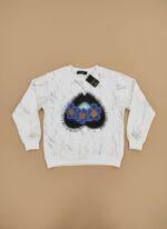 A white kids graphic sweater with a grey marble print, featuring a dark blue heart-shaped graphic with three blue and yellow flowers, lying flat on a beige background.