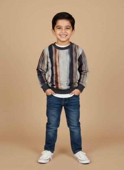 Boy wearing a striped multicolor kids sweater with grey, navy, and brown tones, styled with jeans and sneakers.
