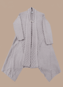 Women's knit sweater with a textured open-front design and a decorative brooch at the collar, in a neutral color.