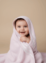 A happy baby with dark hair, wrapped in a pink baby hooded towel with white stripes, smiling at the camera.