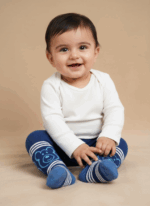 A smiling baby wearing a white long-sleeve bodysuit and blue baby tights with a bear design and white stripes.