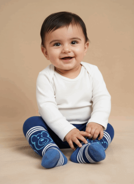 A smiling baby wearing a white long-sleeve bodysuit and blue baby tights with a bear design and white stripes.