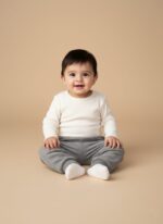 A smiling baby wearing a white long-sleeve top and grey ribbed baby pants with a subtle bear embroidery.