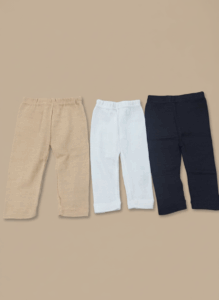 Three pairs of baby pants: one beige, one white, and one black, laid flat on a neutral background.