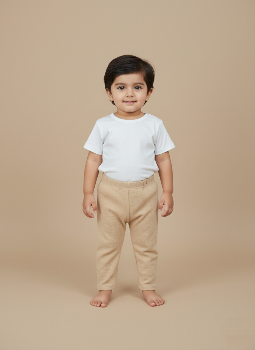 Essential Unisex Baby Pants Set A smiling toddler wearing a white short-sleeve top and beige baby pants, standing on a light brown background.