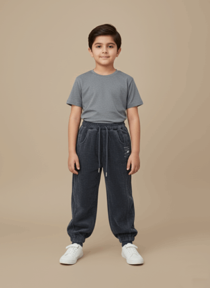 A child wearing a grey t-shirt and grey kids corduroy joggers with white sneakers, standing and smiling.