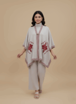 Light grey women's embroidered poncho sweater with burgundy geometric design and border on a light brown background.