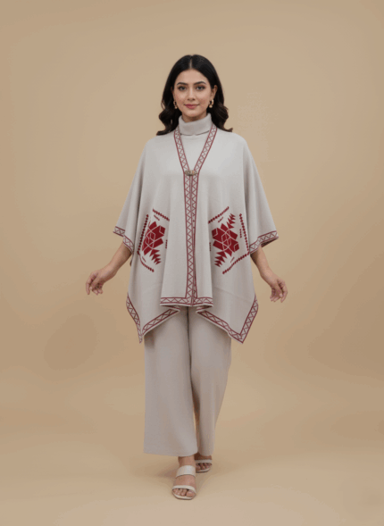 Light grey women's embroidered poncho sweater with burgundy geometric design and border on a light brown background.