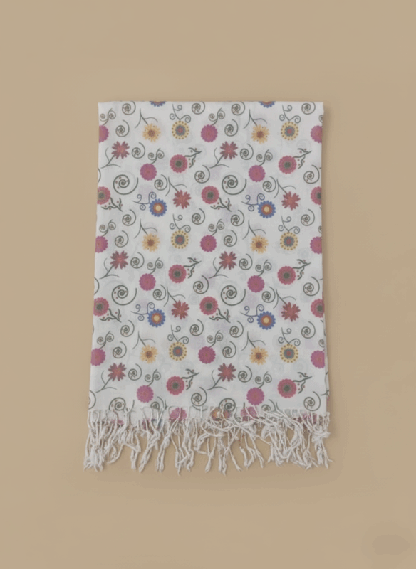 White floral print shawl with colorful flowers, green swirls, and white fringe laid flat on a beige background.