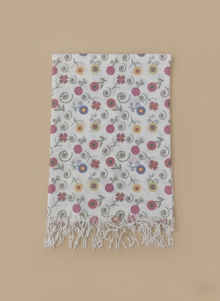 White floral print shawl with colorful flowers, green swirls, and white fringe laid flat on a beige background.