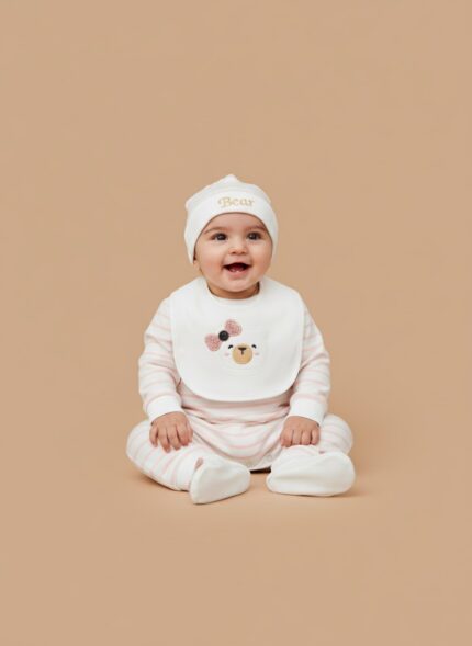 A happy baby girl wearing a pink and white striped "Baby Bear" four-piece starter outfit set, including a knotted hat, a bib with a bear face design, and a long-sleeve jumpsuit.