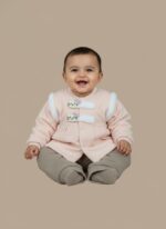 A smiling baby sitting and wearing a pink long-sleeve sweater featuring decorative cat-face buttons and white faux-fur shoulder accents, paired with mocha-colored jogger pants. This is the Baby Cat Detail Sweater Set.