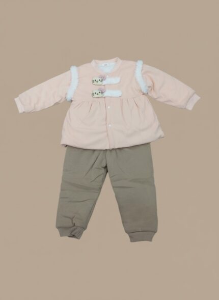A smiling baby sitting and wearing a pink long-sleeve sweater featuring decorative cat-face buttons and white faux-fur shoulder accents, paired with mocha-colored jogger pants. This is the Baby Cat Detail Sweater Set.
