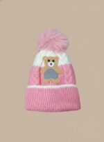 A knitted baby hat in shades of grey and white with a pink bear appliqué on the front and a large, fluffy grey faux fur pompom on top.