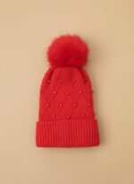 A knitted baby hat in shades of grey and white with a pink bear appliqué on the front and a large, fluffy grey faux fur pompom on top.