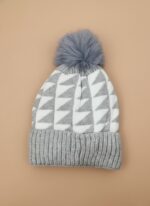 A knitted baby hat in shades of grey and white with a pink bear appliqué on the front and a large, fluffy grey faux fur pompom on top.