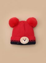 A knitted baby hat in shades of grey and white with a pink bear appliqué on the front and a large, fluffy grey faux fur pompom on top.