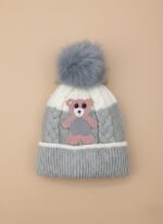 A knitted baby hat in shades of grey and white with a pink bear appliqué on the front and a large, fluffy grey faux fur pompom on top.