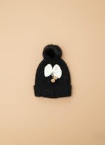 A knitted baby hat in shades of grey and white with a pink bear appliqué on the front and a large, fluffy grey faux fur pompom on top.