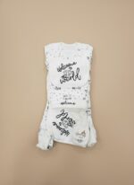 Lay-flat studio shot of the complete "Welcome to the World" baby starter outfit set, showing a white and black polka dot onesie, pants, bib, and knotted hat, laid out neatly.