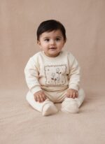A happy baby sitting and smiling, wearing a cream long-sleeve sweater with a delicate square frame floral embroidery design on the chest, paired with matching cream jogger pants. This is the Baby Floral Embroidered Sweater Set.