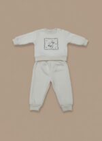 A happy baby sitting and smiling, wearing a cream long-sleeve sweater with a delicate square frame floral embroidery design on the chest, paired with matching cream jogger pants. This is the Baby Floral Embroidered Sweater Set.