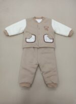 A smiling baby sitting, dressed in a quilted beige long-sleeve sweater with cream sleeves, an embroidered teddy bear on the chest, and decorative plaid-lined pockets, paired with matching quilted beige pants. This is the Baby Quilted Teddy Bear Sweater Set.