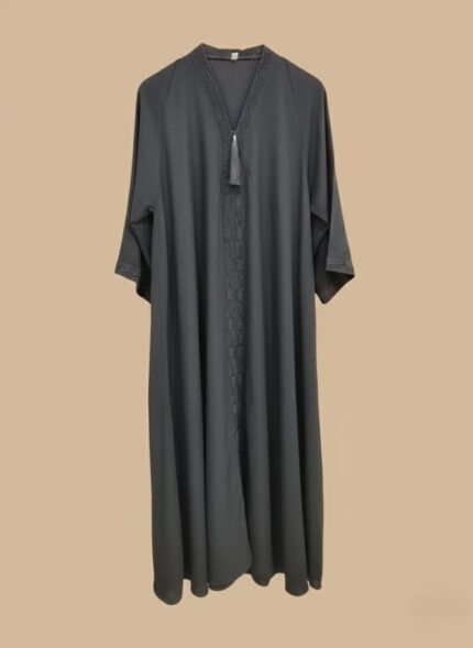 A woman in a full-length black abaya with subtle beading along the V-neck and down the front, accented with a black tassel.