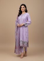 Full-length view of a woman wearing a lavender cotton embroidered suit with a dupatta, standing against a beige background. The suit has intricate floral embroidery on the hem and sleeves.