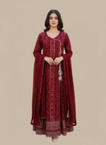 A woman wearing a vibrant maroon printed chiffon Anarkali style suit with a long-sleeved, flared kurta, matching maroon trousers, and a coordinating chiffon dupatta. The suit has intricate gold and silver prints and a decorative tassel.