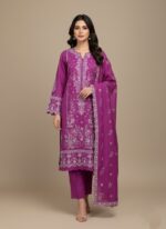 A woman wearing a vibrant purple embroidered lawn suit with a long-sleeved shirt and matching trousers and dupatta. The suit features detailed white floral embroidery and scalloped edges.