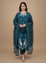 Full-length image of a woman wearing an embroidered cotton teal suit with detailed white floral embroidery on the tunic and trousers, paired with a matching printed dupatta. The outfit is made of lawn and is suitable for formal occasions.
