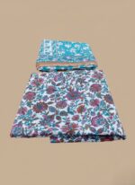 Two folded sets of 3 PC unstitched lawn fabric, one with a prominent pink and teal floral pattern on white, and another smaller teal fabric with white and orange floral motifs, displayed on a wooden table in a retail setting.