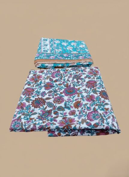 Two folded sets of 3 PC unstitched lawn fabric, one with a prominent pink and teal floral pattern on white, and another smaller teal fabric with white and orange floral motifs, displayed on a wooden table in a retail setting.