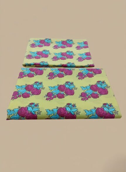 A neatly folded 3 PC unstitched lawn fabric set with a yellow background and bold pink and blue floral patterns, displayed on a wooden table.