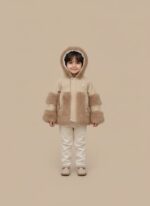Front view of a young child wearing a beige Kids Faux Fur Trim Jacket with a hood, featuring fluffy brown faux fur on the sleeves, front pockets, and hood lining, against a plain background.
