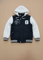 Front view of a black and white Kids Varsity Puffer Jacket with a white hood and sleeves, a black body, and white "GABS" text and a large "G" graphic, worn by a child against a plain background.