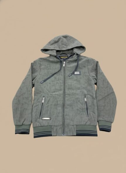 Close-up of a smiling Pakistani toddler wearing an olive green zip-up hooded jacket on a light brown background. Kids casual wear.