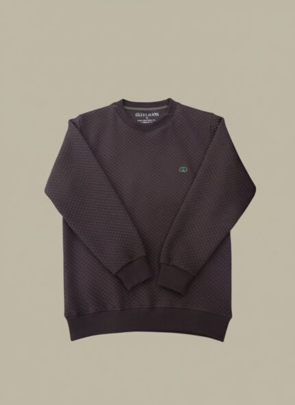 Overhead view of a dark charcoal quilted crewneck sweater with a small green logo and "GLCEI JEANS" tag, highlighting the pattern.