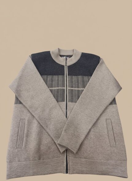 A man wearing a men's color block full zip sweater in light grey and dark charcoal grey with a full zipper, dark blue jeans, and white sneakers, standing against a plain background.