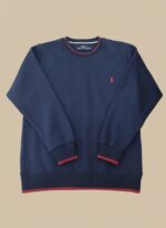 Men's navy crew neck sweater with red striped trim on the collar, cuffs, and hem, worn by a model.