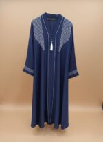 A woman wearing a navy blue abaya with white embroidered lines on the shoulders and down the front, featuring a white tassel at the V-neck.